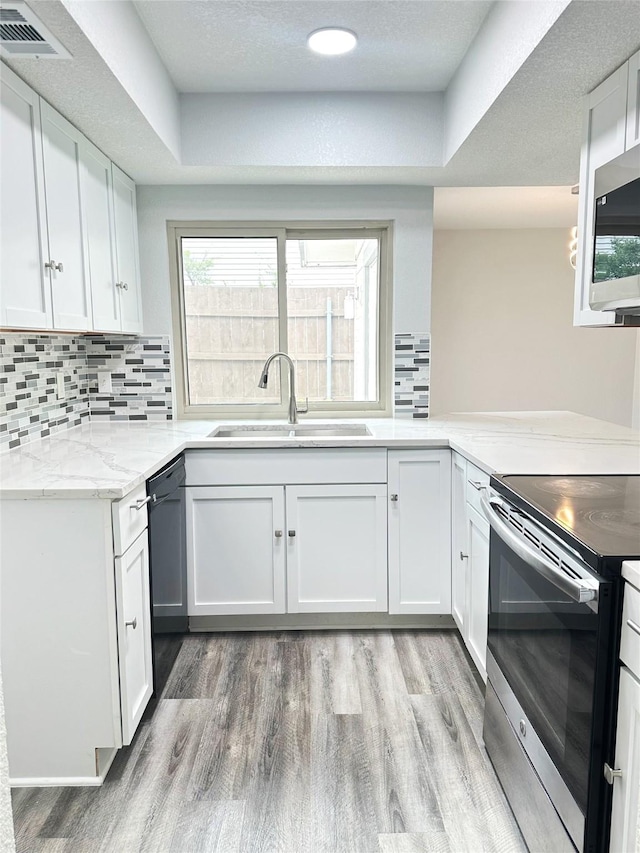 kitchen featuring backsplash, visible vents, appliances with stainless steel finishes, a sink, and light wood-style floors
