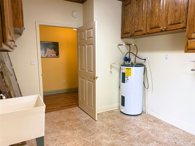 laundry area featuring baseboards, cabinet space, and water heater