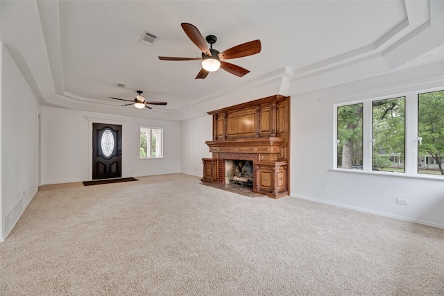 unfurnished living room featuring visible vents, light carpet, ceiling fan, a raised ceiling, and a fireplace with flush hearth