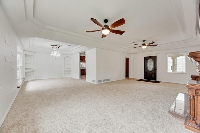 unfurnished living room featuring ceiling fan with notable chandelier, built in features, a tray ceiling, and carpet flooring