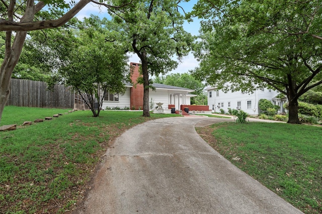 ranch-style house with fence, a chimney, concrete driveway, and a front yard