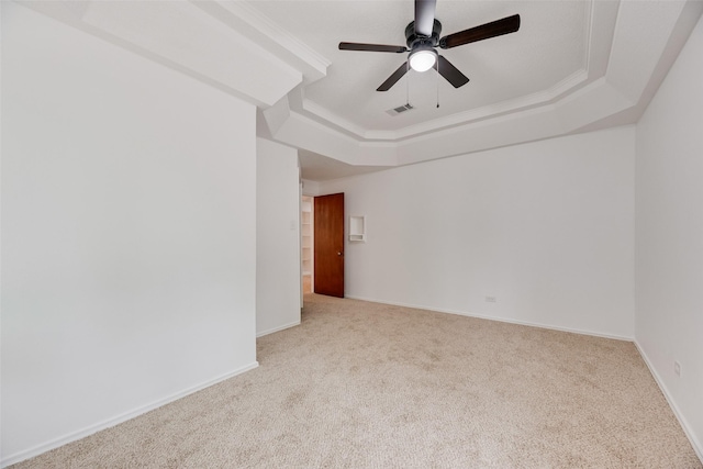 carpeted empty room featuring a raised ceiling, ceiling fan, baseboards, and visible vents