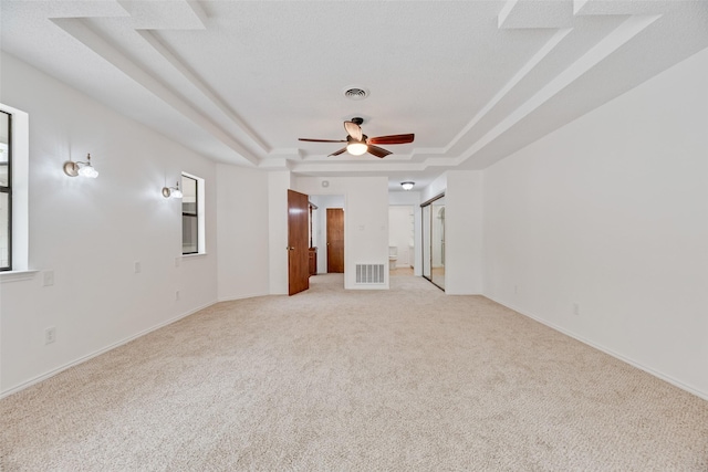 spare room with light colored carpet, a raised ceiling, ceiling fan, and visible vents