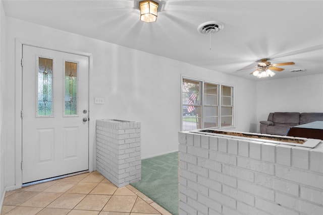 foyer entrance with a ceiling fan, light colored carpet, visible vents, and light tile patterned floors