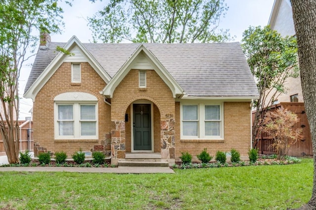 english style home featuring brick siding, fence, and a front yard