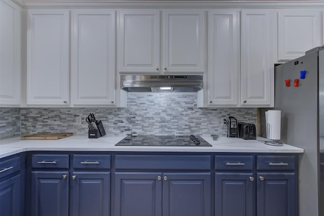 kitchen featuring freestanding refrigerator, black electric cooktop, under cabinet range hood, tasteful backsplash, and blue cabinets
