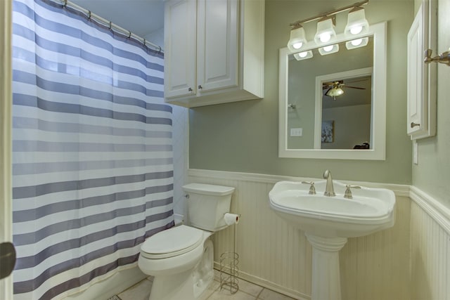 full bath with toilet, tile patterned floors, a shower with shower curtain, and a wainscoted wall