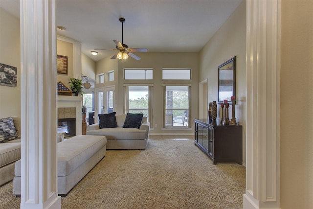 living area featuring a tiled fireplace, baseboards, ceiling fan, and light carpet