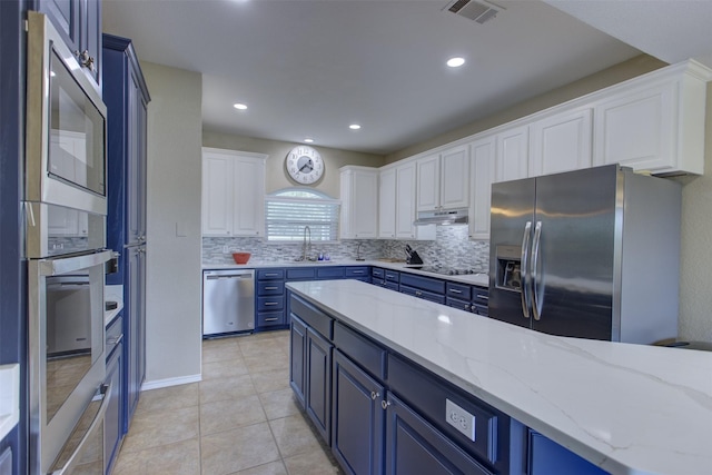 kitchen with appliances with stainless steel finishes, under cabinet range hood, blue cabinetry, and visible vents