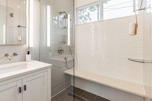 full bathroom featuring vanity, tiled shower, and tile walls
