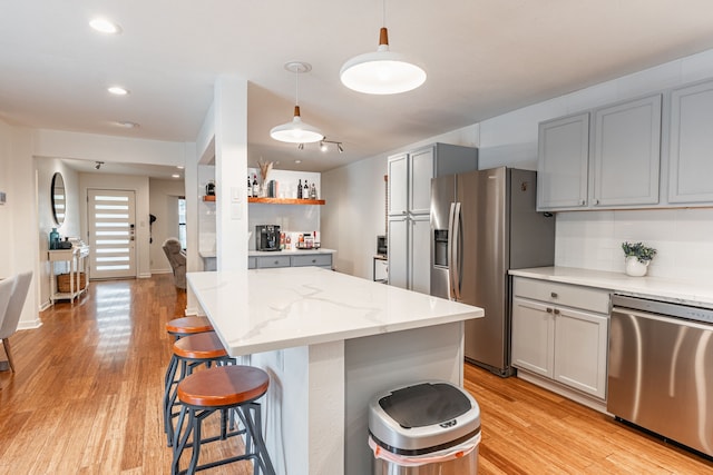kitchen with light wood-style floors, appliances with stainless steel finishes, a breakfast bar area, and gray cabinetry
