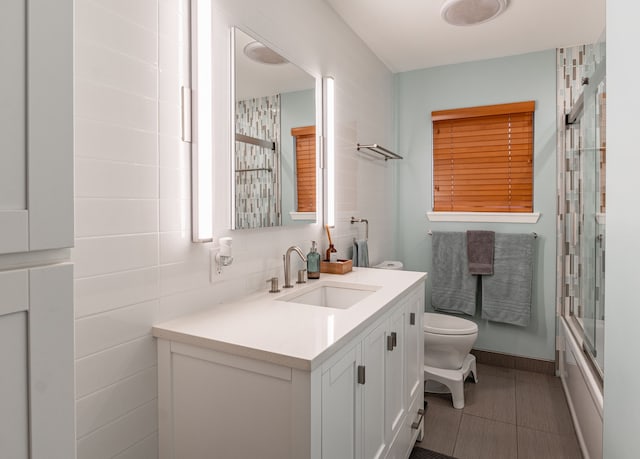 full bath featuring baseboards, vanity, tile patterned floors, bath / shower combo with glass door, and toilet