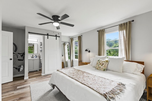 bedroom featuring ceiling fan, light wood-type flooring, a barn door, baseboards, and connected bathroom