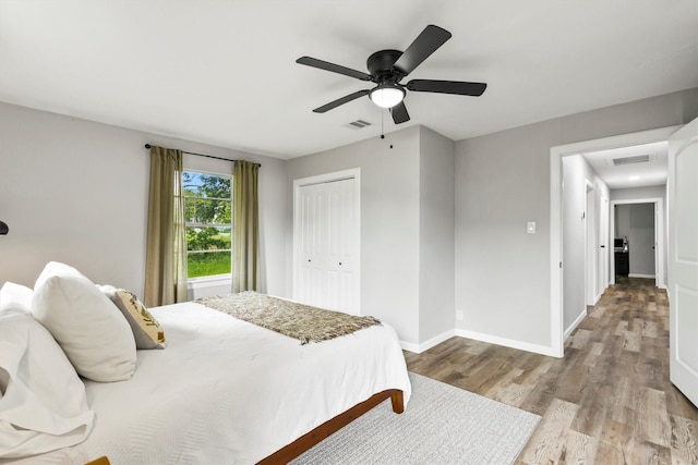 bedroom with visible vents, a closet, wood finished floors, baseboards, and a ceiling fan