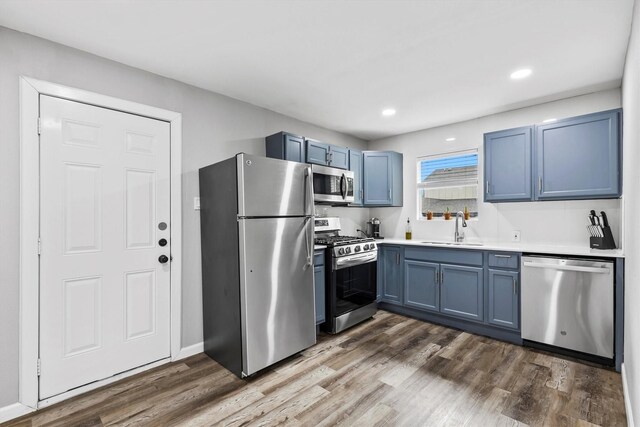 kitchen with dark wood-style flooring, a sink, light countertops, blue cabinetry, and stainless steel appliances