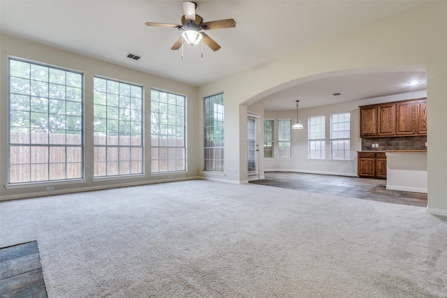 unfurnished living room with ceiling fan, carpet floors, arched walkways, baseboards, and visible vents