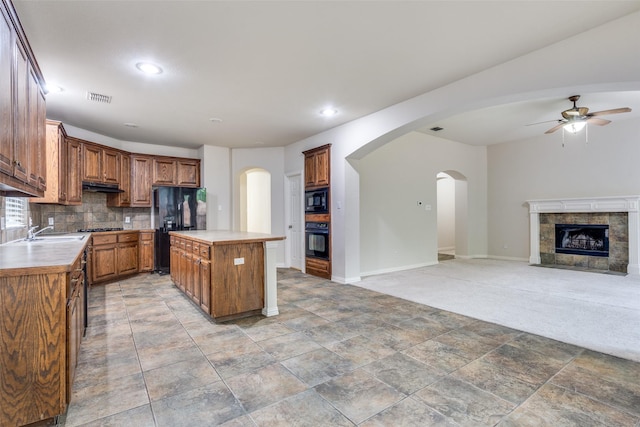kitchen with decorative backsplash, a ceiling fan, a center island, black appliances, and under cabinet range hood