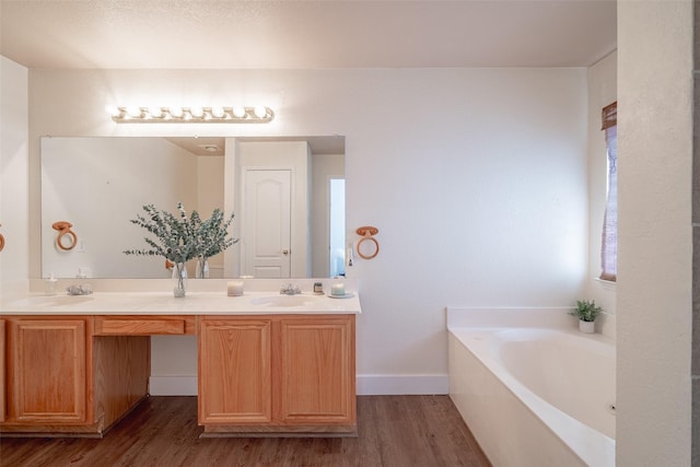 bathroom with double vanity, a bath, wood finished floors, a sink, and baseboards