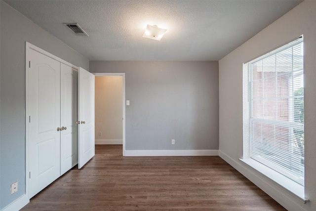 unfurnished bedroom with a textured ceiling, baseboards, visible vents, and dark wood-style floors
