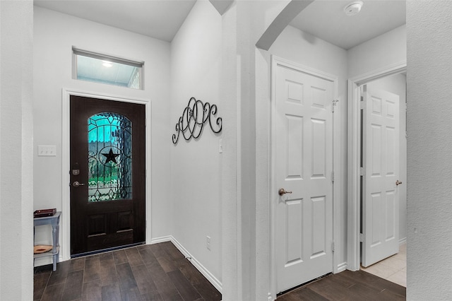 foyer entrance featuring baseboards, arched walkways, and wood finished floors