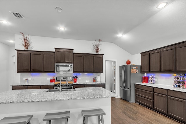 kitchen featuring decorative backsplash, a kitchen breakfast bar, visible vents, vaulted ceiling, and stainless steel appliances