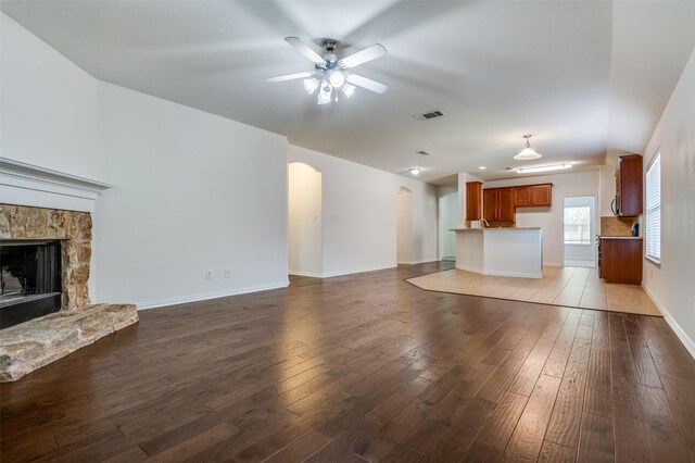unfurnished living room with visible vents, wood-type flooring, a ceiling fan, a stone fireplace, and arched walkways