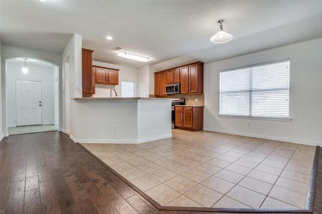 kitchen with appliances with stainless steel finishes, arched walkways, brown cabinetry, a peninsula, and baseboards