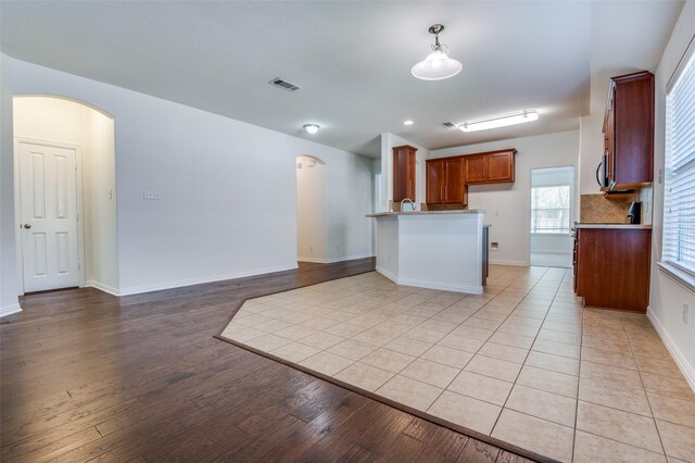 kitchen with light wood-style floors, arched walkways, brown cabinetry, open floor plan, and visible vents