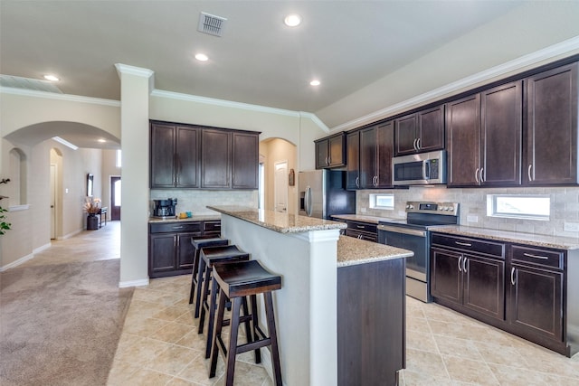 kitchen with appliances with stainless steel finishes, ornamental molding, a kitchen bar, and arched walkways