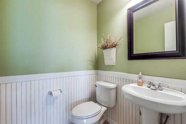 bathroom featuring toilet, a sink, and a wainscoted wall