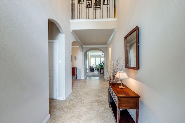 hall featuring crown molding, arched walkways, baseboards, and a high ceiling