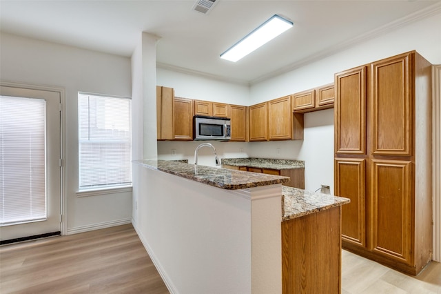 2372 Homewood Ln, Grand Prairie, TX 75050 - kitchen featuring stainless steel microwave, light stone countertops, a peninsula, brown cabinetry, and light wood-type flooring