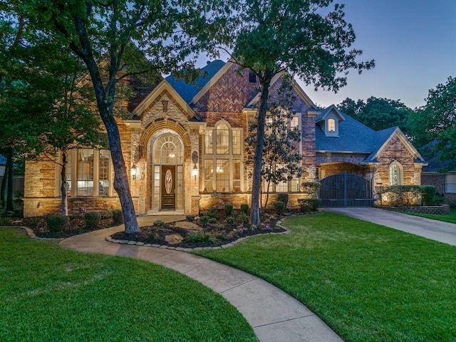 view of front of home with driveway, a yard, brick siding, and stone siding