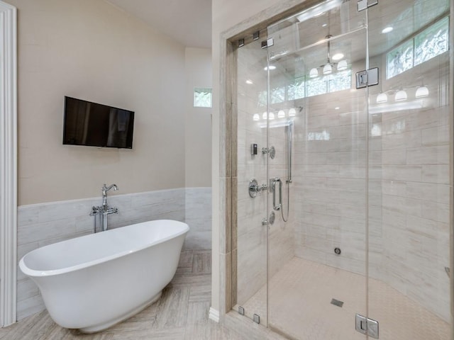 bathroom featuring a freestanding tub, a stall shower, a wainscoted wall, and tile walls