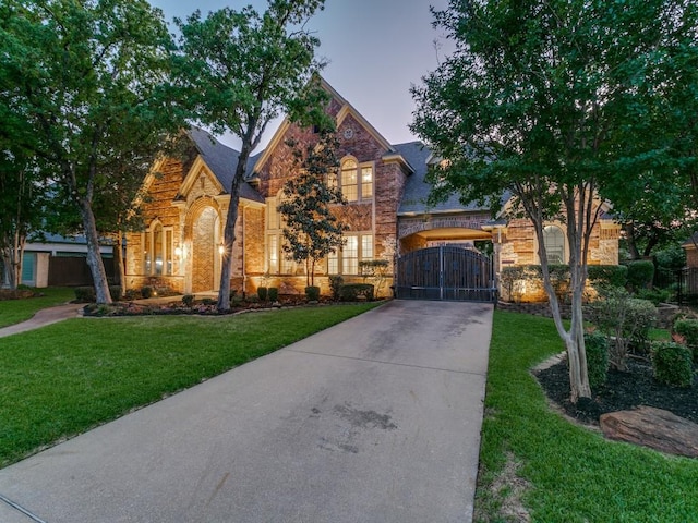 view of front of house with driveway, stone siding, a gate, brick siding, and a yard
