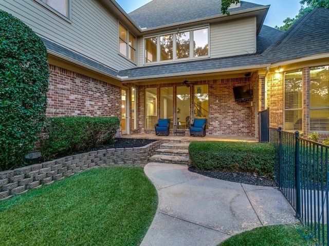 view of exterior entry featuring brick siding, a patio, and a shingled roof