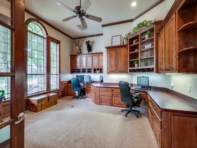 office area with built in desk, crown molding, light colored carpet, and a ceiling fan