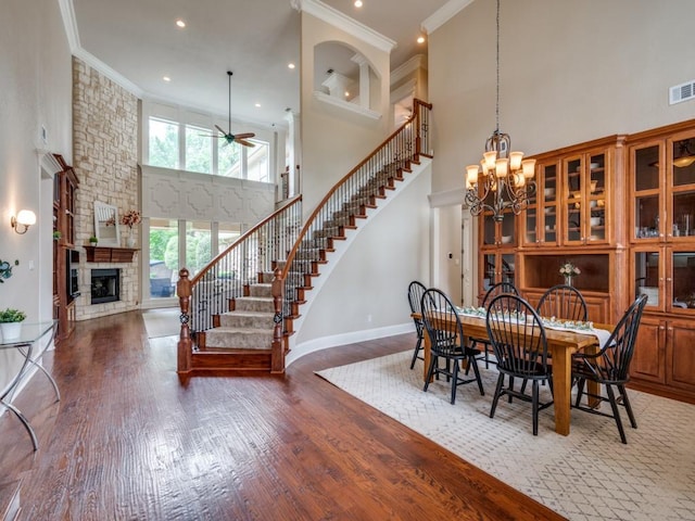 dining area with a high ceiling, a fireplace, stairway, wood finished floors, and ceiling fan