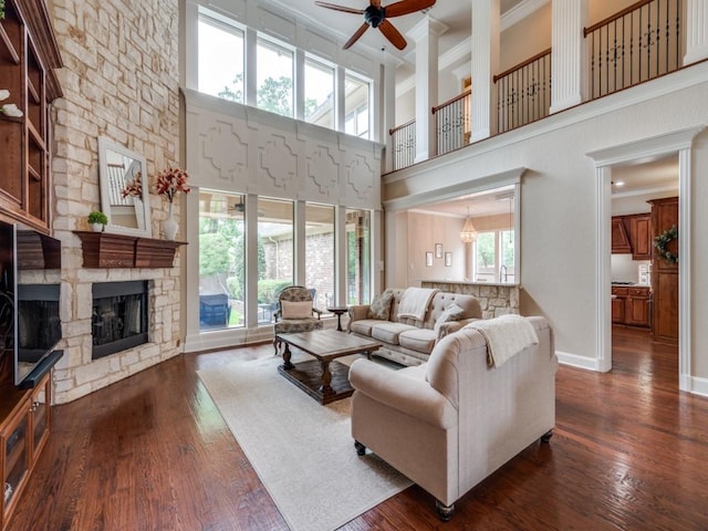 living area featuring ornamental molding, ceiling fan, dark wood finished floors, a stone fireplace, and baseboards