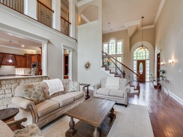 living room with ornamental molding, a high ceiling, wood finished floors, stairs, and baseboards