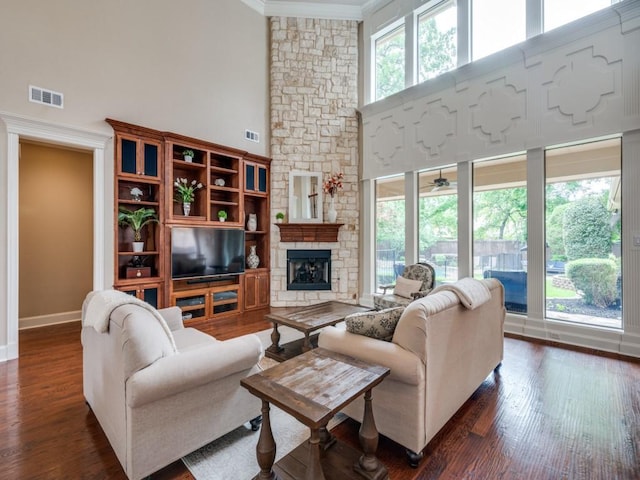 living room with crown molding, a high ceiling, wood finished floors, baseboards, and a stone fireplace