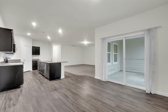 kitchen with a sink, light countertops, open floor plan, wood finished floors, and a center island with sink