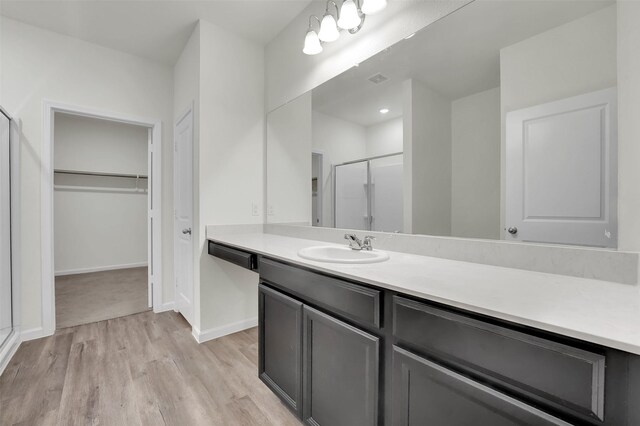 full bath featuring vanity, baseboards, a shower stall, wood finished floors, and a spacious closet