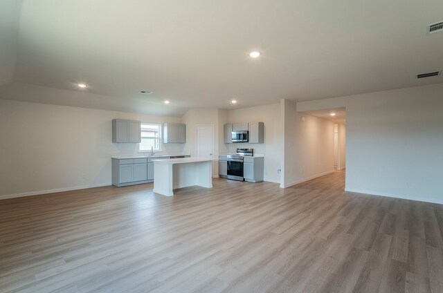 unfurnished living room featuring a sink, light wood-style floors, recessed lighting, baseboards, and visible vents