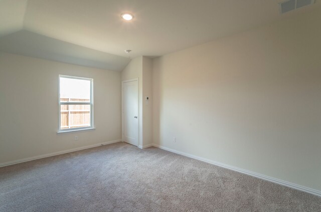 spare room with carpet floors, baseboards, visible vents, and vaulted ceiling
