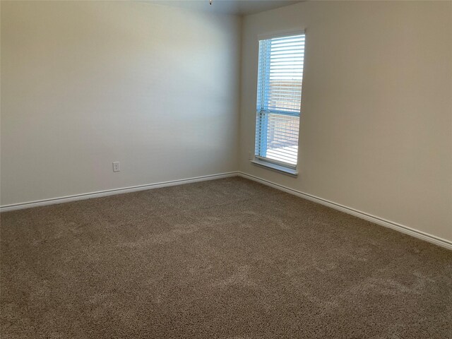 unfurnished room featuring baseboards, a healthy amount of sunlight, and dark colored carpet
