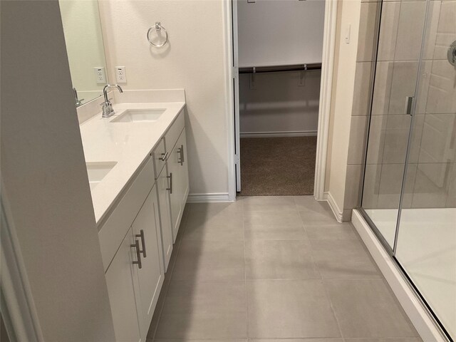 bathroom featuring tile patterned flooring, double vanity, baseboards, a sink, and a stall shower
