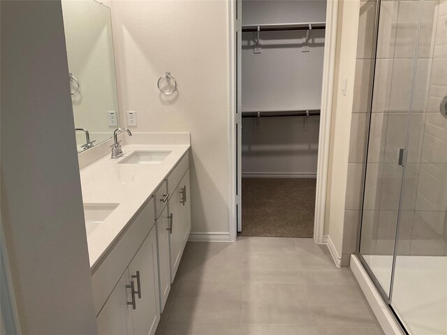 bathroom featuring a walk in closet, a sink, double vanity, baseboards, and a stall shower