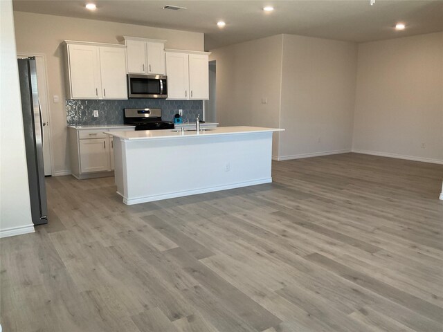 kitchen with a kitchen island with sink, recessed lighting, tasteful backsplash, light wood-style flooring, and appliances with stainless steel finishes
