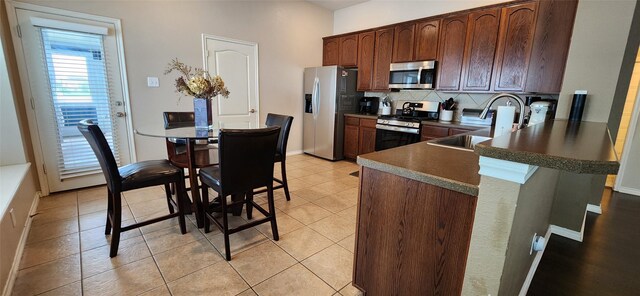 kitchen with decorative backsplash, a peninsula, dark countertops, a sink, and stainless steel appliances
